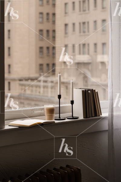 Stock image of window looking out to urban building with a window sill with notebook, candles, coffee and books.