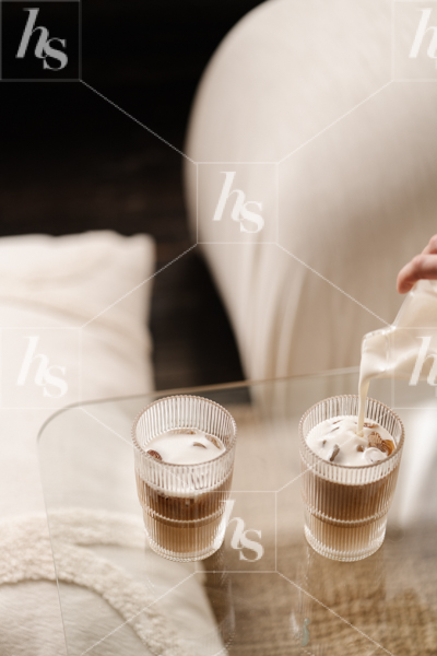 Stock image featuring woman pouring milk into iced coffee.