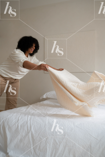 Interior design image featuring woman tossing sheet to make bed. Stock images for female entrepreneurs.