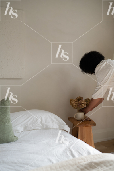 Stock image featuring interior designer placing vase of flowers in bedroom for decor.