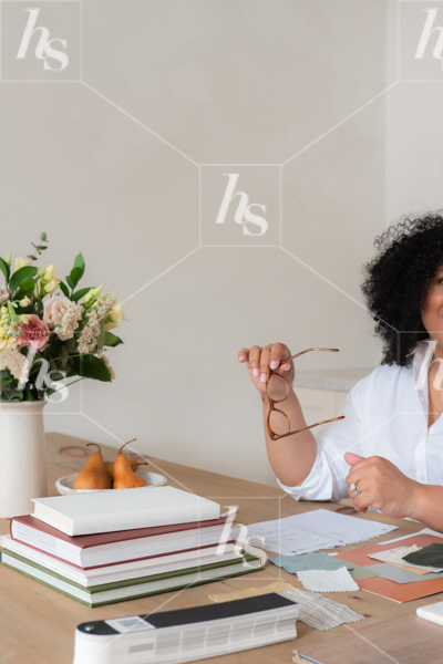 Interior design stock image featuring designer planning out decor at desk with glasses, notebooks, pears and flowers.