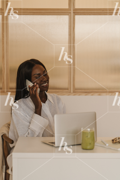 A woman talking on the phone while looking at her laptop in this workspace stock photo collection