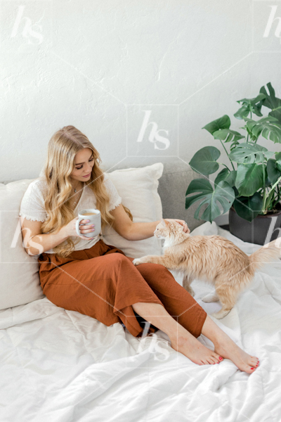 Woman in burnt orange on bed petting cat in our mindfulness stock photography collection