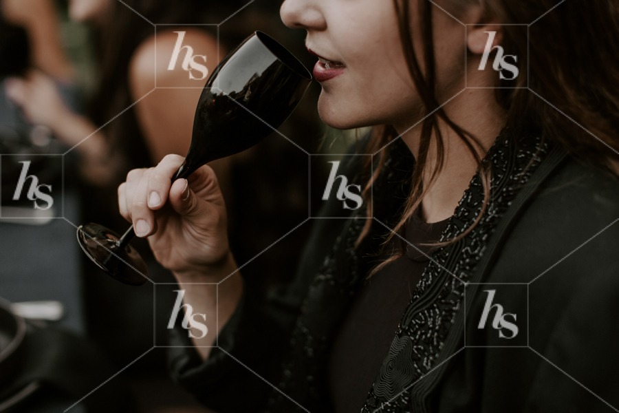 Stock image featuring woman drinking out a black wine glass.