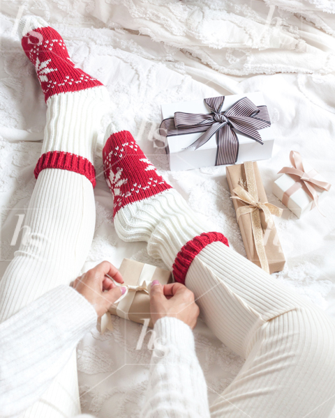 Stock photo of woman wearing read and white cosy socks, wrapping presents on bed