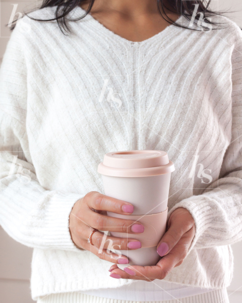 Woman in a cosy white sweater holding a pair cup of coffee