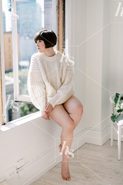 Woman in cozy beige sweater sitting on the window sill of her apartment