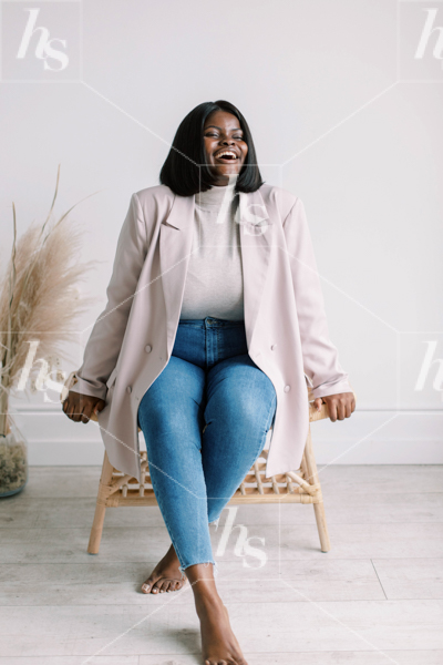 Plus size African American woman sitting happily on a wicker chair wearing denim and casual jacket in neutral colors