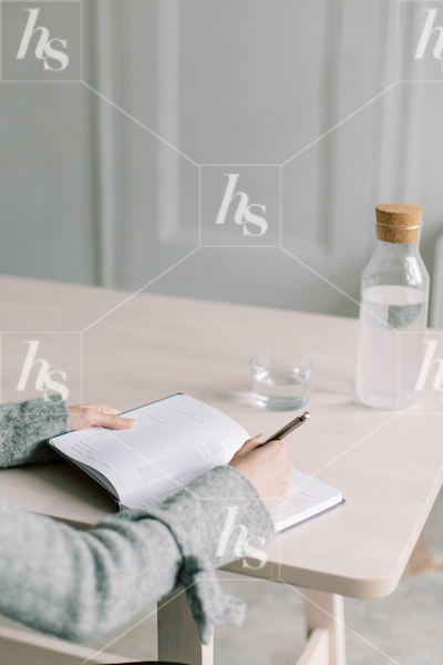Styled lifestyle photo by Haute Stock of a woman journaling on a clean neutral desk next to a water bottle