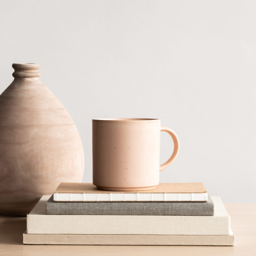 Stock photo of peach mug mockup on a stack of books next to a vase, perfect for product designer