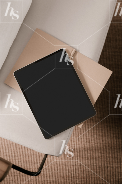 Flatlay of iPad mockup on edge of open notebook and couch, part of Haute Stock tech and stationery mockups collection
