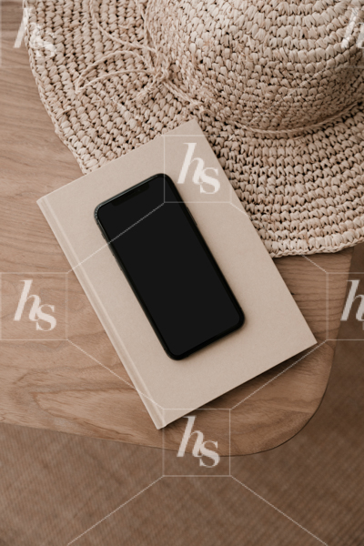 Styled image of phone mockup on top of book with straw hat