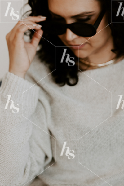 Styled stock image of woman dressed in neutral color sweater, wearing sunglasses looking down