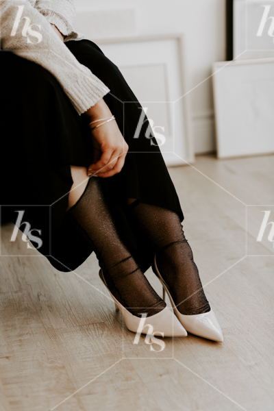 Minimal fashion stock photo of woman dressed in black adjusting her sheer stockings