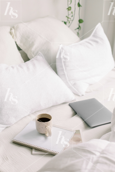Cozy workspace stock image featuring laptop, notebook and coffee on bed.