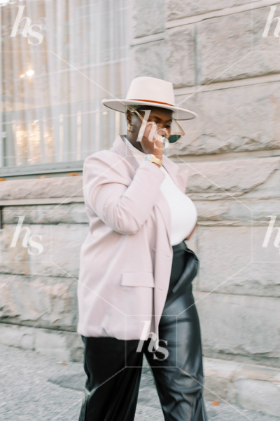 Styled stock image of plus size woman in blush blazer and black pants walking next to a building
