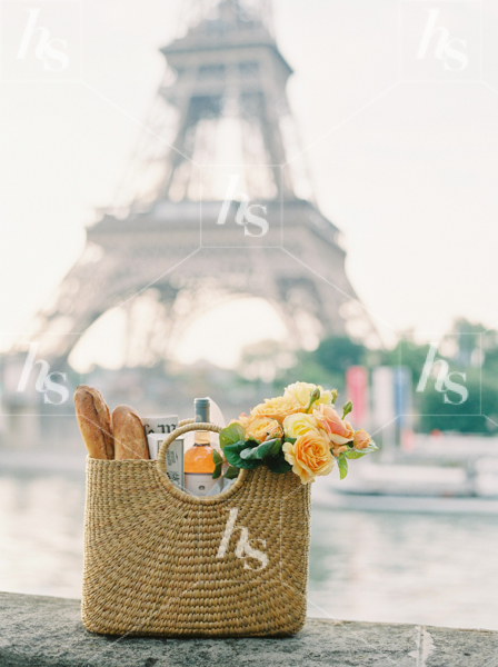 Romantic stock photo of a picnic basket of roses and baguettes with the Eiffel Tower in the background, perfect for Valentine's Day.