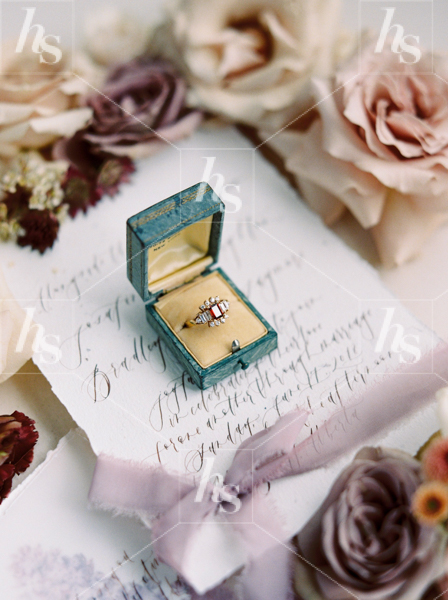 Styled stock image of wedding ring in box on invitation surrounded by flowers