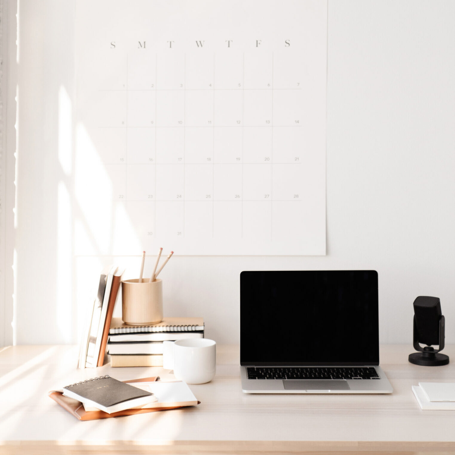 Styled stock photo of well organized desk with laptop, notebooks and monthly planner on the wall.