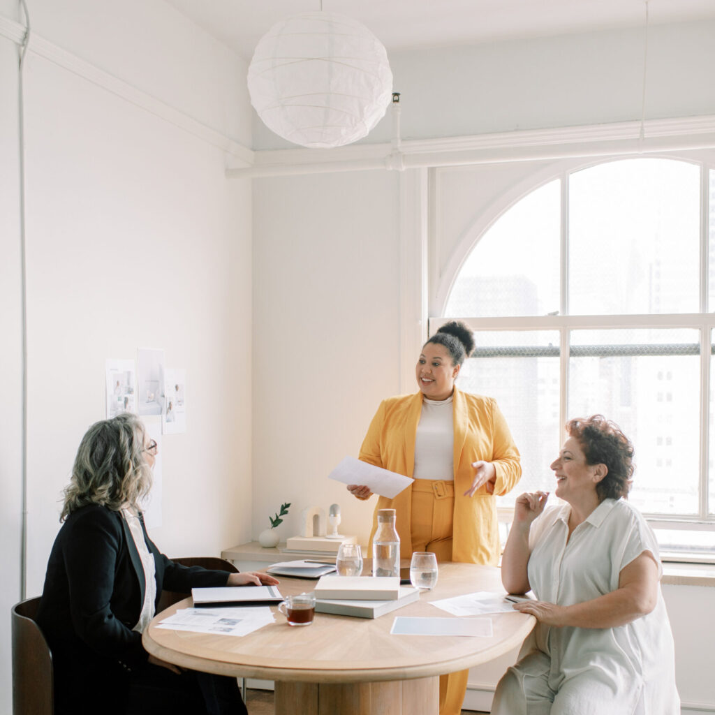 Collaboration stock photo of three women entrepreneurs meeting in a mid-century style office.
