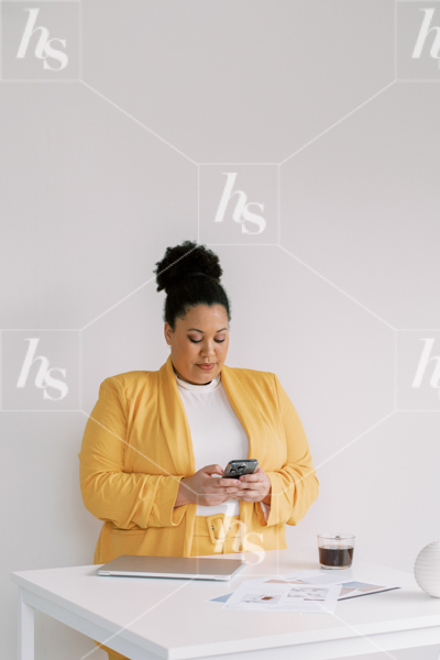 Woman entrepreneur dressed in yellow, working on phone in front of desk