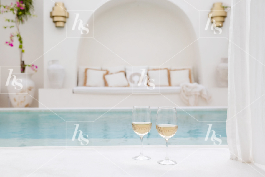 Styled stock image of glasses of wine by a pool.