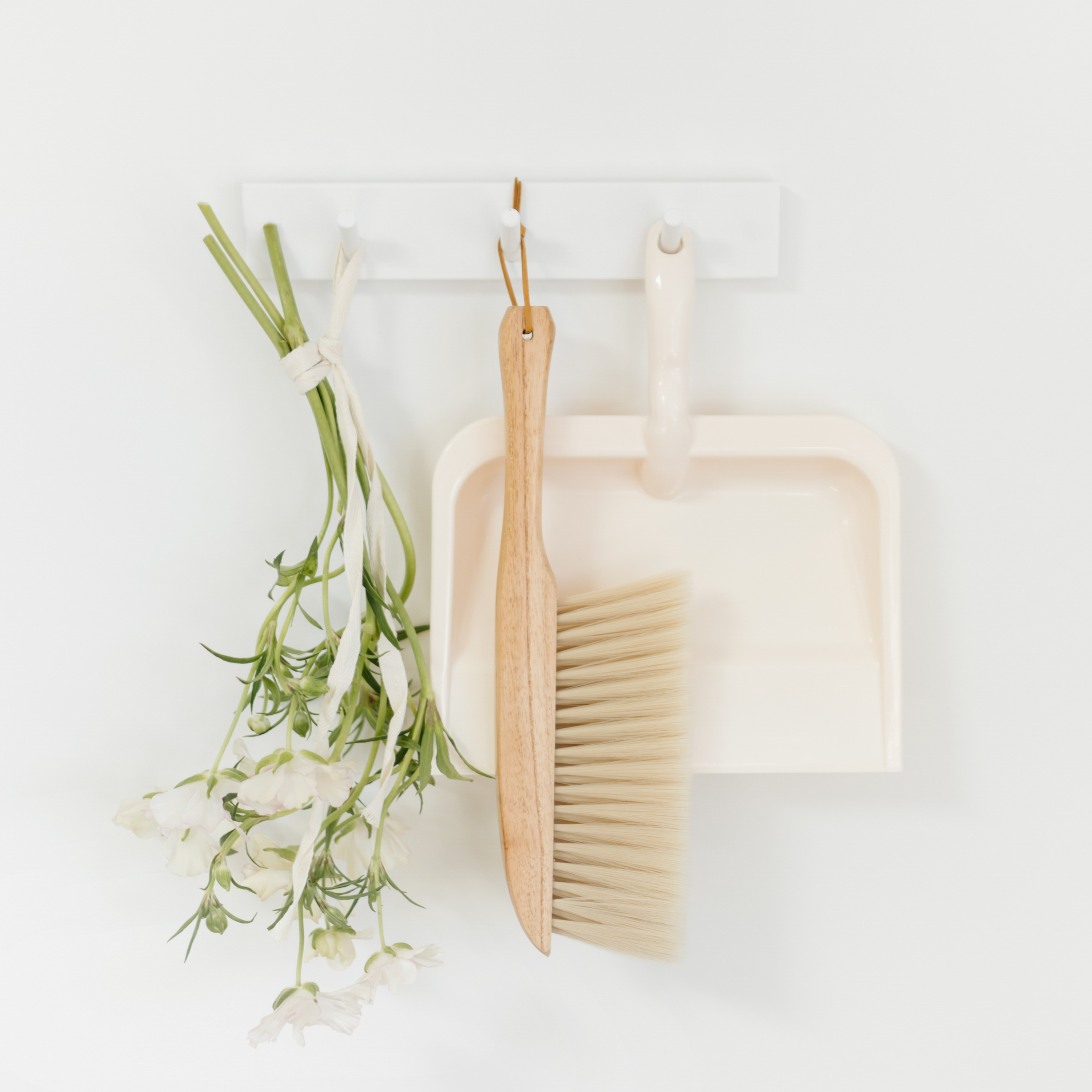 Florals, dust pan, and small broom hanging from wall, a styled stock image perfect for home organizing brands
