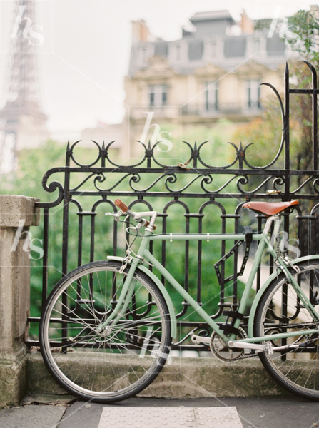 Stock photo of green vintage bike secured to fence with Eiffel Tower in background