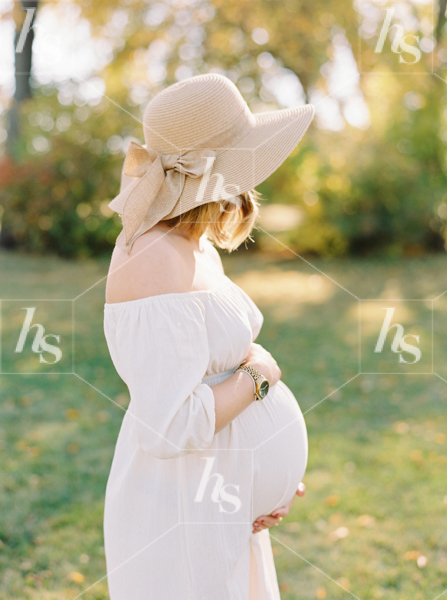 Stock image of woman enjoying the sun in the park while holding her baby bump