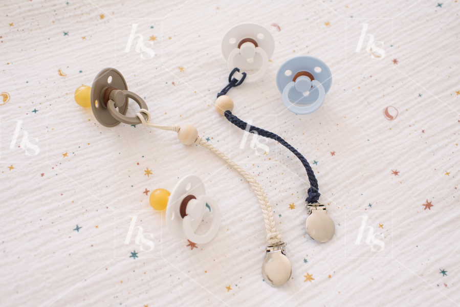 Styled stock photo of a collection of pacifiers on baby sheets. Motherhood stock image.