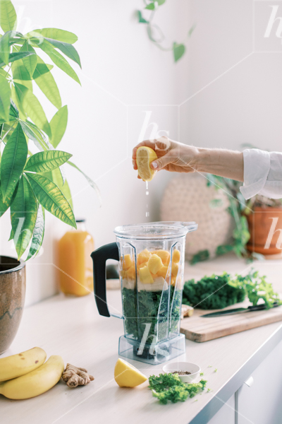 health and wellness stock photo featuring woman squeezing lemon into a green smoothie