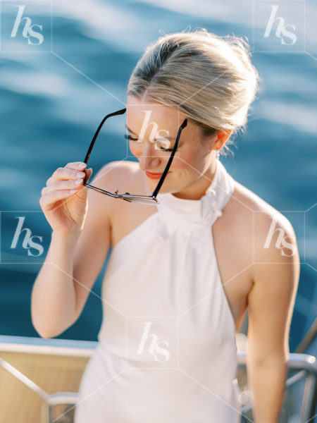 Chic woman putting her sunglasses on with blue sea water in the background. 