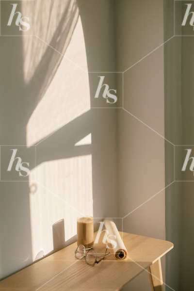 Minimal stock image of paper roll, coffee, and glasses on desk with shadows on wall