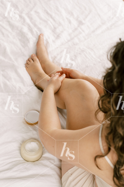 Beauty stock photo featuring a woman in bed applying cream on legs.