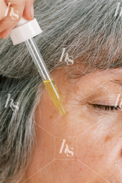 Older woman applying serum on face, part of Haute Stock's Ageless Beauty Collection.