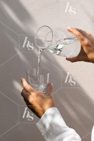 A woman pouring a glass of water from decanter, a self-care stock photo from Linen collection.