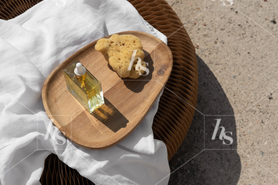 Serum and bath sponge on wooden tray on top of pouf, a perfect self-are self-care stock photo to elevate your beauty & wellness brand.