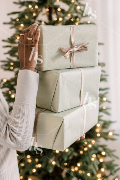 A woman holding a stack of wrapped gifts in front of the Christmas tree, part of the holiday stock photos and videos collection by Haute Stock