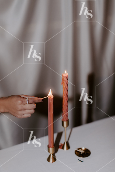 Woman lighting tall red candles, part of Ladies' night moody NYE stock imagery collection.