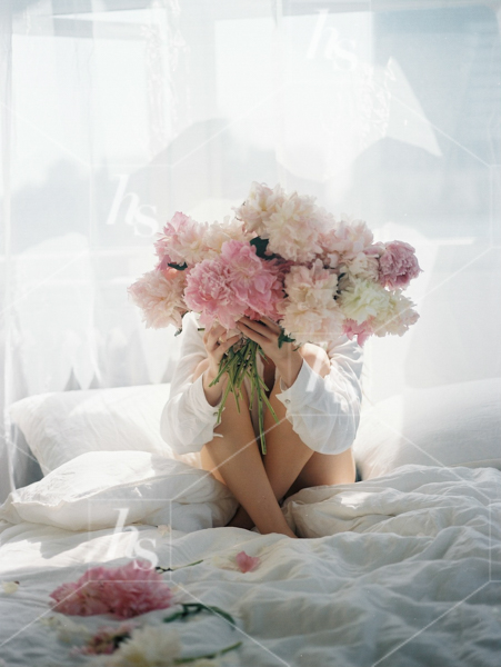 Woman sitting on bed and covering her face with a large bouquet of peonies, part of Haute Stock's Bed of Peonies, floral stock photos & videos collection.