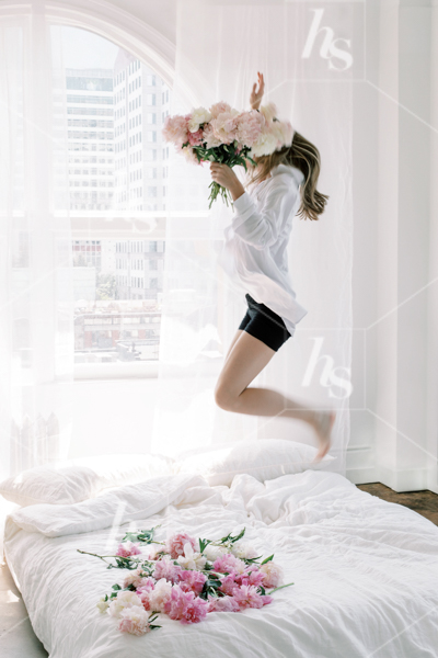 Woman jumping on bed of peonies while holding a bouquet of peonies, part of Haute Stock's Bed of Peonies, floral stock photos & videos collection.