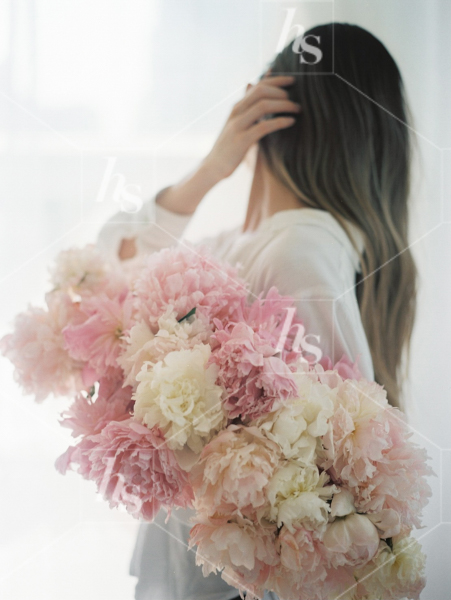 Woman holding a large bouquet of peonies as she hides her face from the camera, part of Haute Stock's Bed of Peonies, floral stock photos & videos collection.