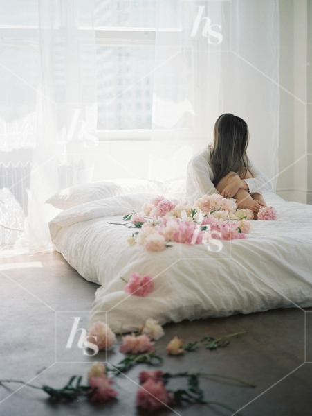 Woman sitting on bed with peonies surrounding her, part of Haute Stock's Bed of Peonies, floral stock photos & videos collection.