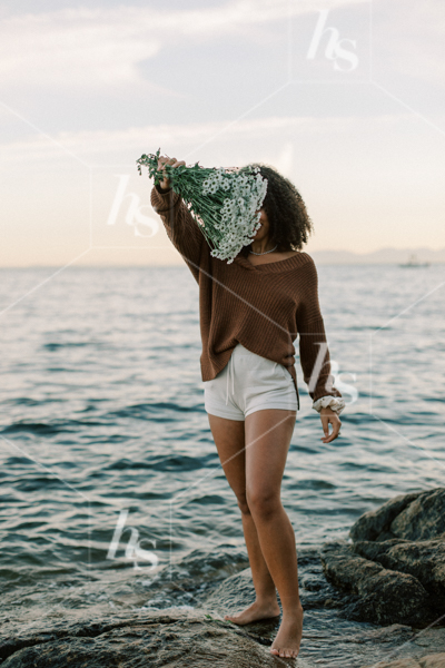 Woman holding a bouquet of flowers in front of her at the beach, part of Sips at Sunset a fun stock photos & videos collection by Haute Stock