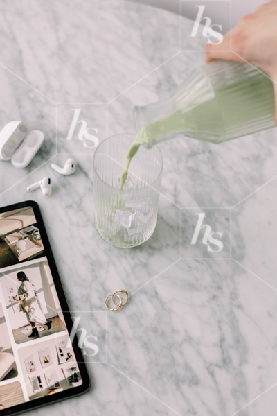 Woman pouring matcha into cup beside iPad with mood board, AirPods, and earrings, part of Matcha Time: green workspace stock photos & videos collection
