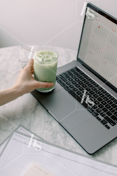 Woman reaching for her matcha as she schedules and plans, part of Matcha Time: green workspace stock photos & videos collection