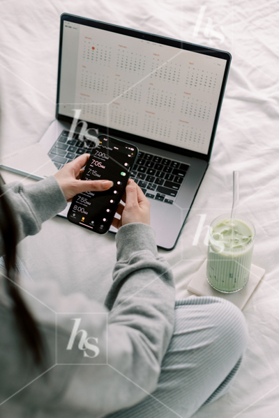 Woman setting her alarm as she works on her laptop in bed, part of Matcha Time: green workspace stock photos & videos collection