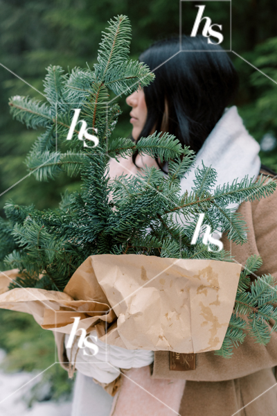 Woman holding a bunch of evergreen branches, part of Snow Day winter holiday stock images collection by Haute Stock