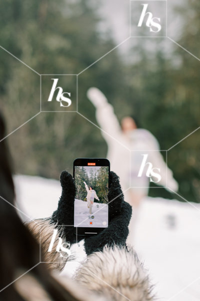 Woman recording her friend in the snow, part of Snow Day winter holiday stock images collection by Haute Stock