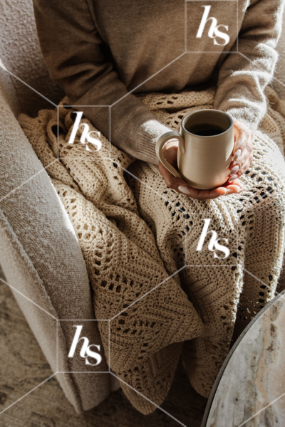 A cozy scene of a model sitting on a chair with coffee and blanket, part of home interiors stock image collection: Haven